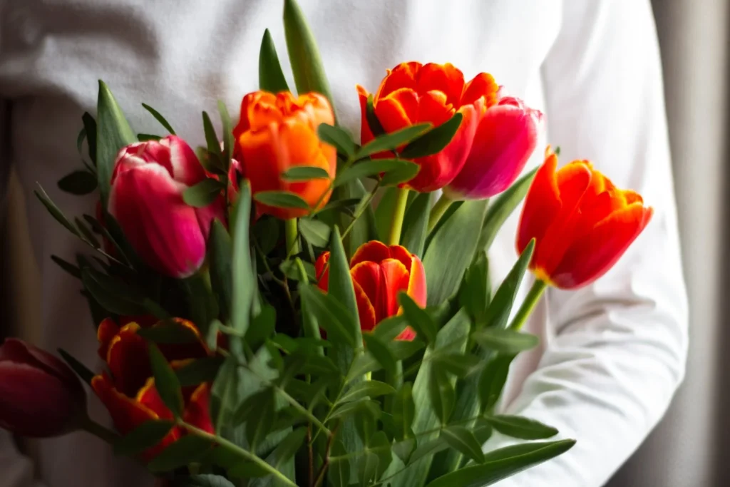 Vibrant bouquet of red and orange flowers held by a person in white.